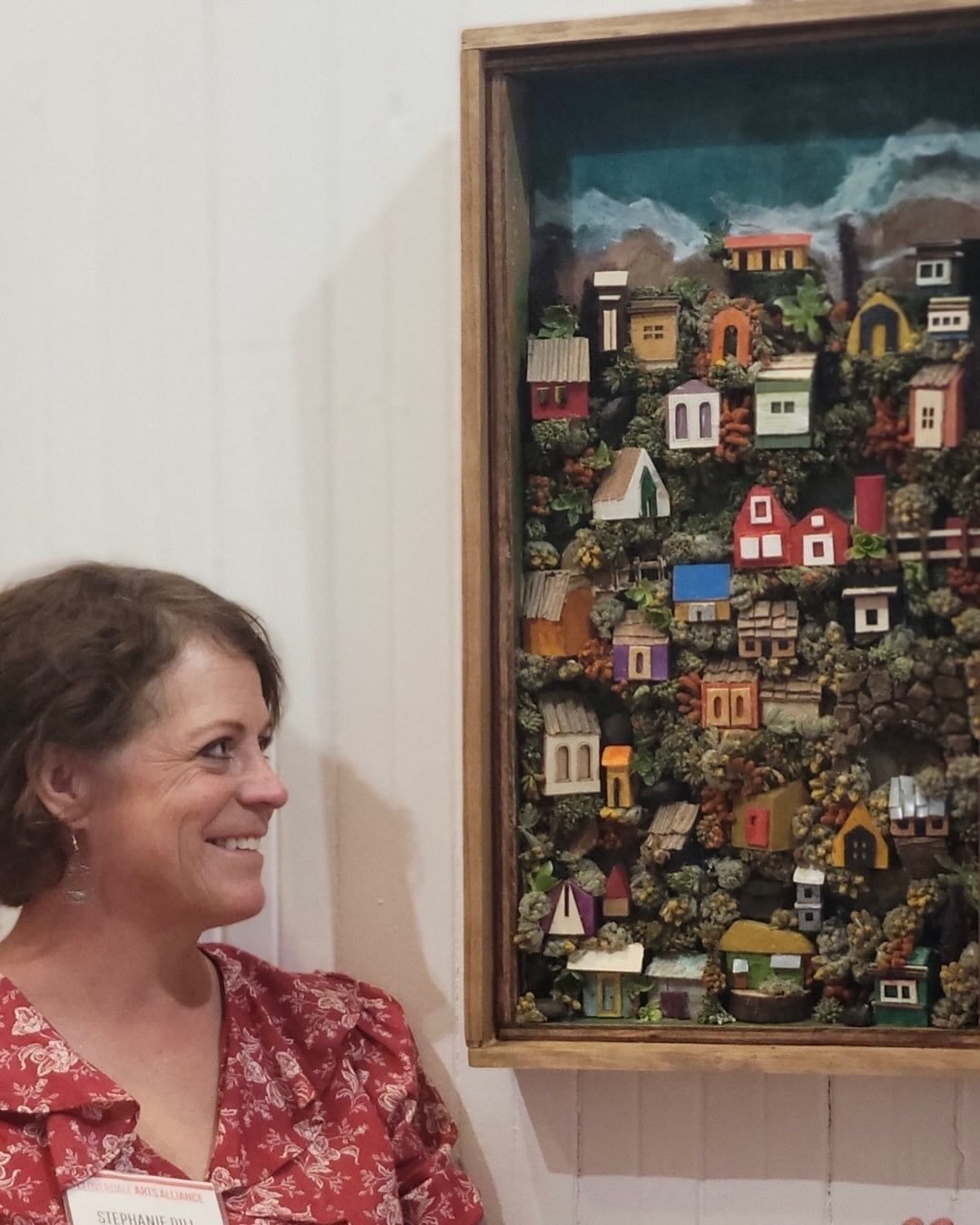 Stephanie Dill smiling beside one of her miniature town shadow boxes