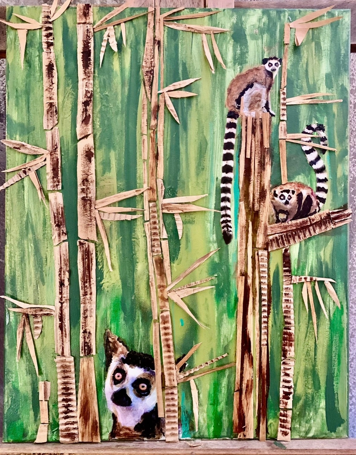 Three ring-tailed lemurs among raised bamboo stems on a green painted background